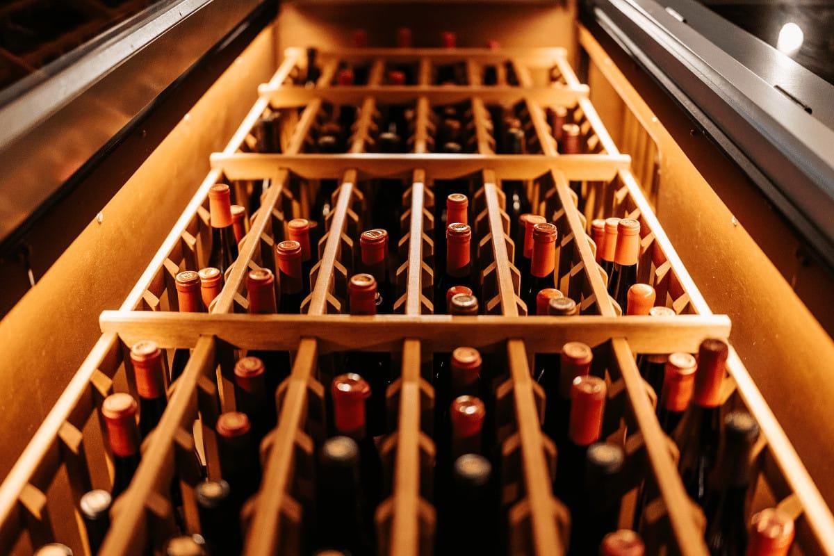 Red Wine Guide: Malbec Wine vs Cabernet Sauvignon 4 Rows of red wine bottles resting on wooden racks in a warmly lit wine cellar