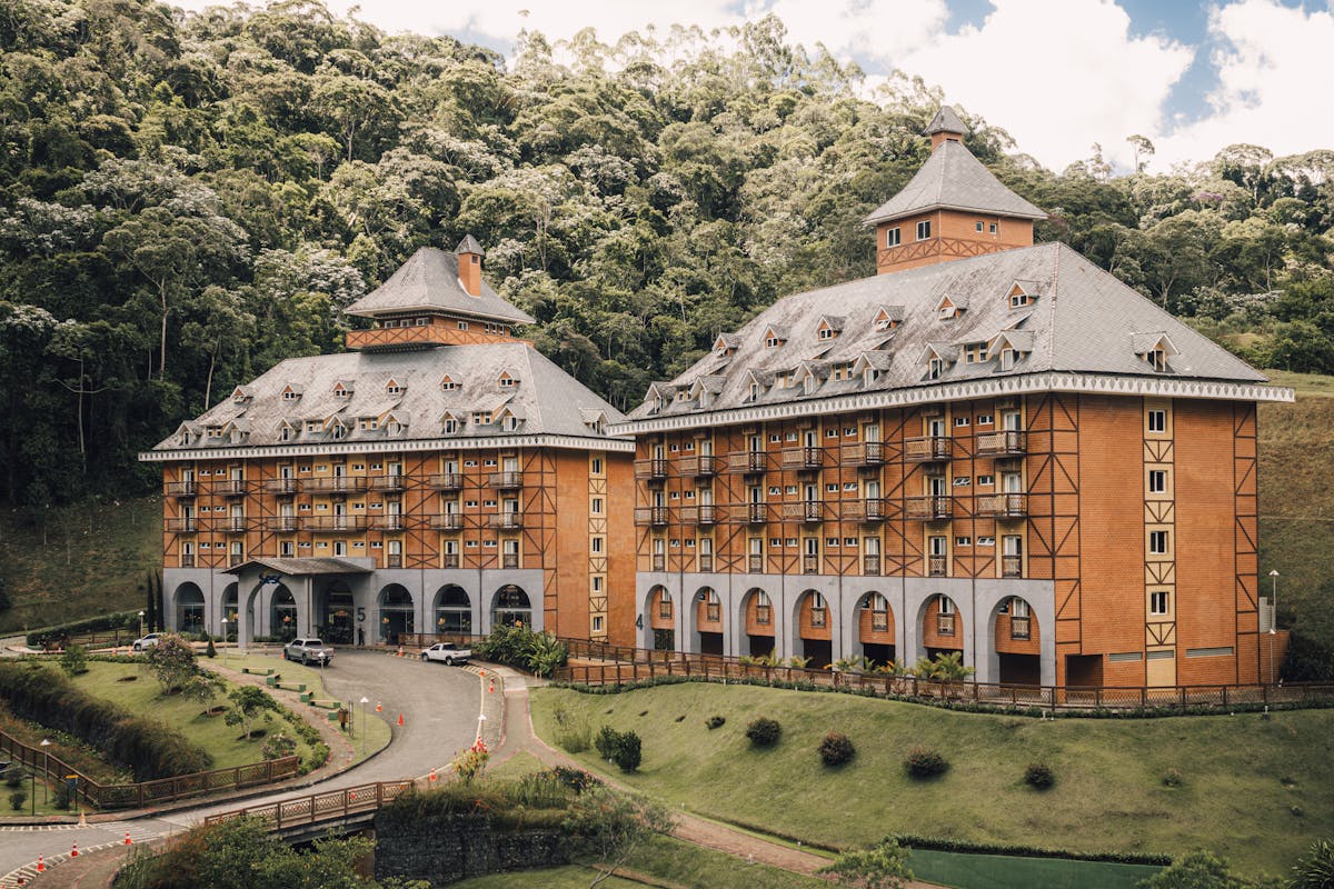 A picturesque Bavarian-style hotel surrounded by lush greenery and forest hillside.
