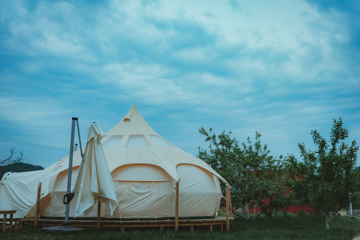 Glamping Zion National Park: The Ultimate Escape 2 A beautiful cream-colored glamping tent set amid lush green trees under a vibrant blue sky.
