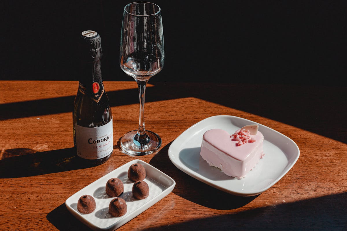 Heart-shaped cake and chocolates with champagne on a wooden table, ideal for celebrations.