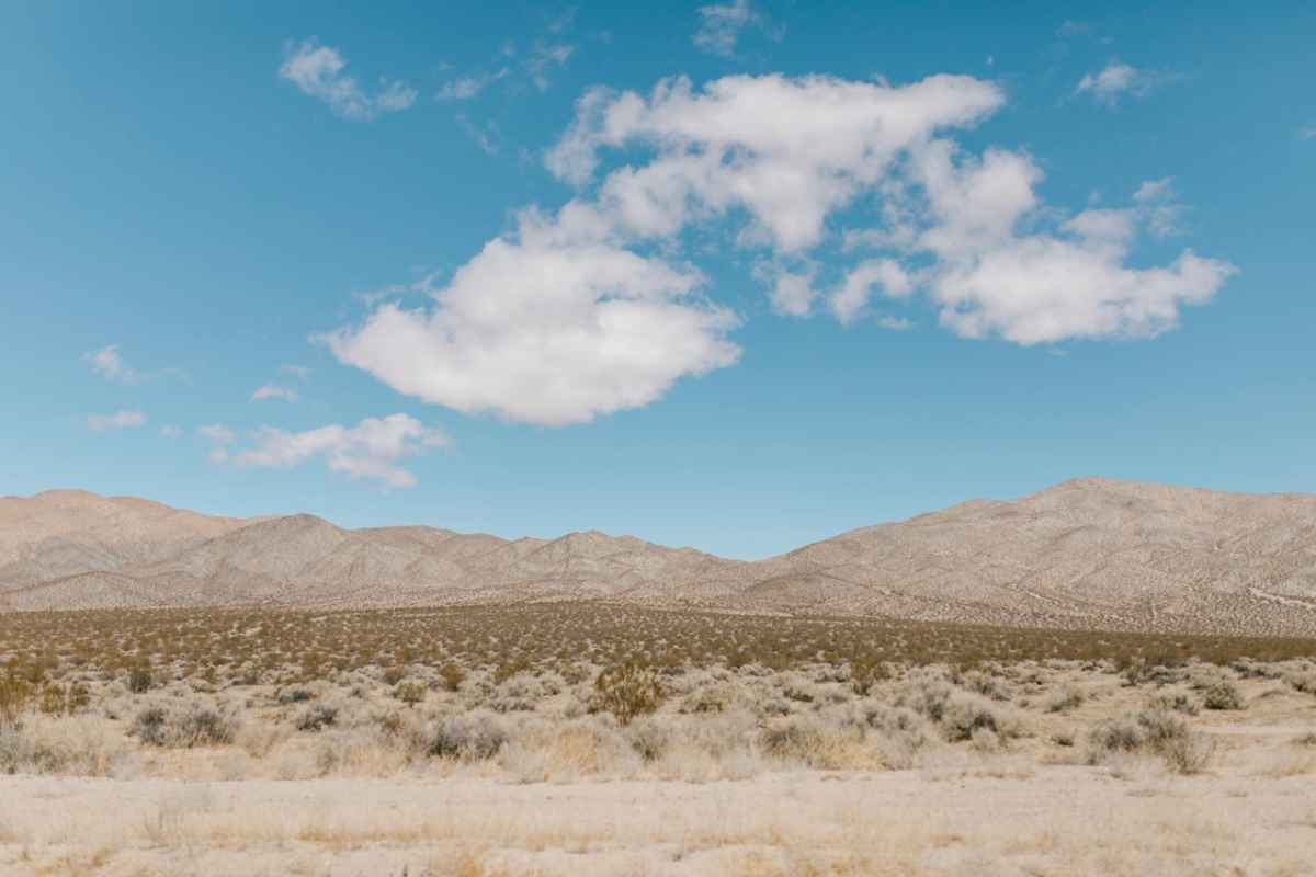Vast desert landscape under a bright blue sky with scattered white clouds.