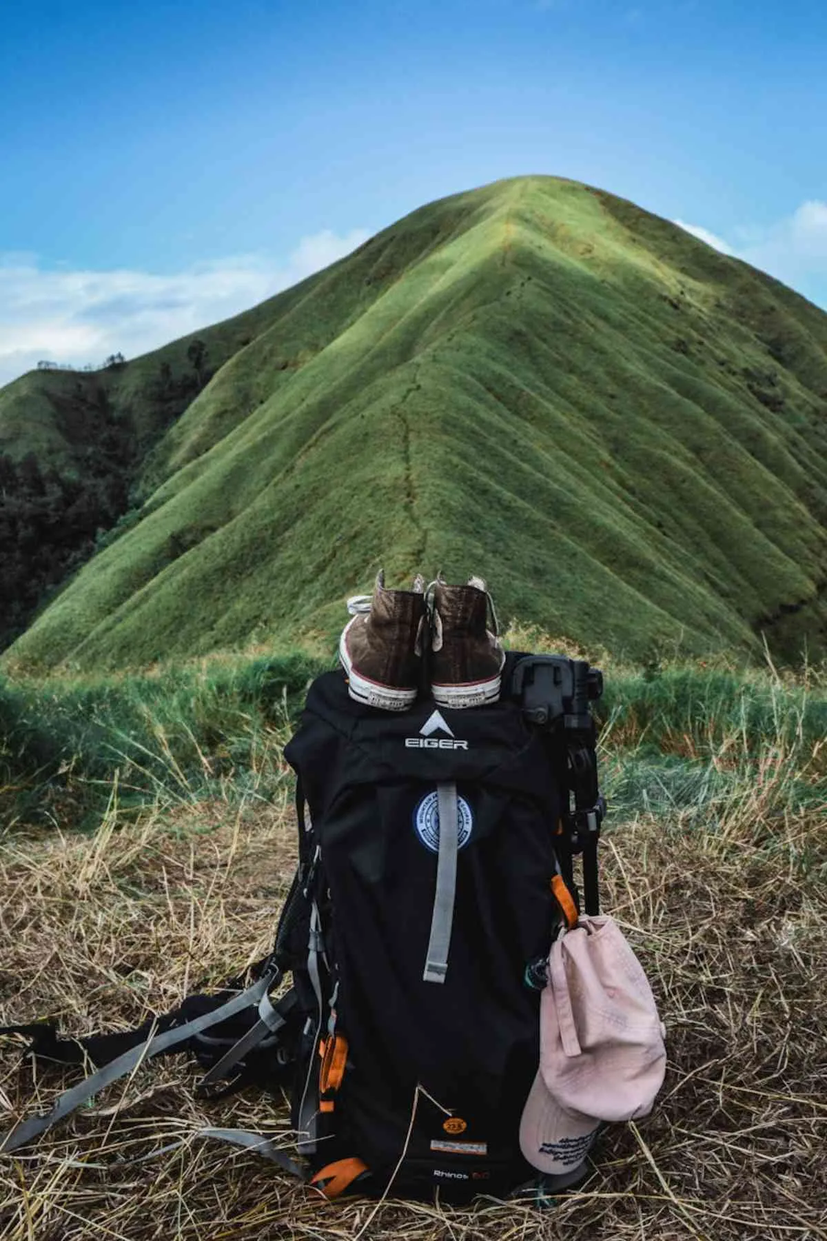 Hiking backpack with footwear and cap against lush green mountain adventure