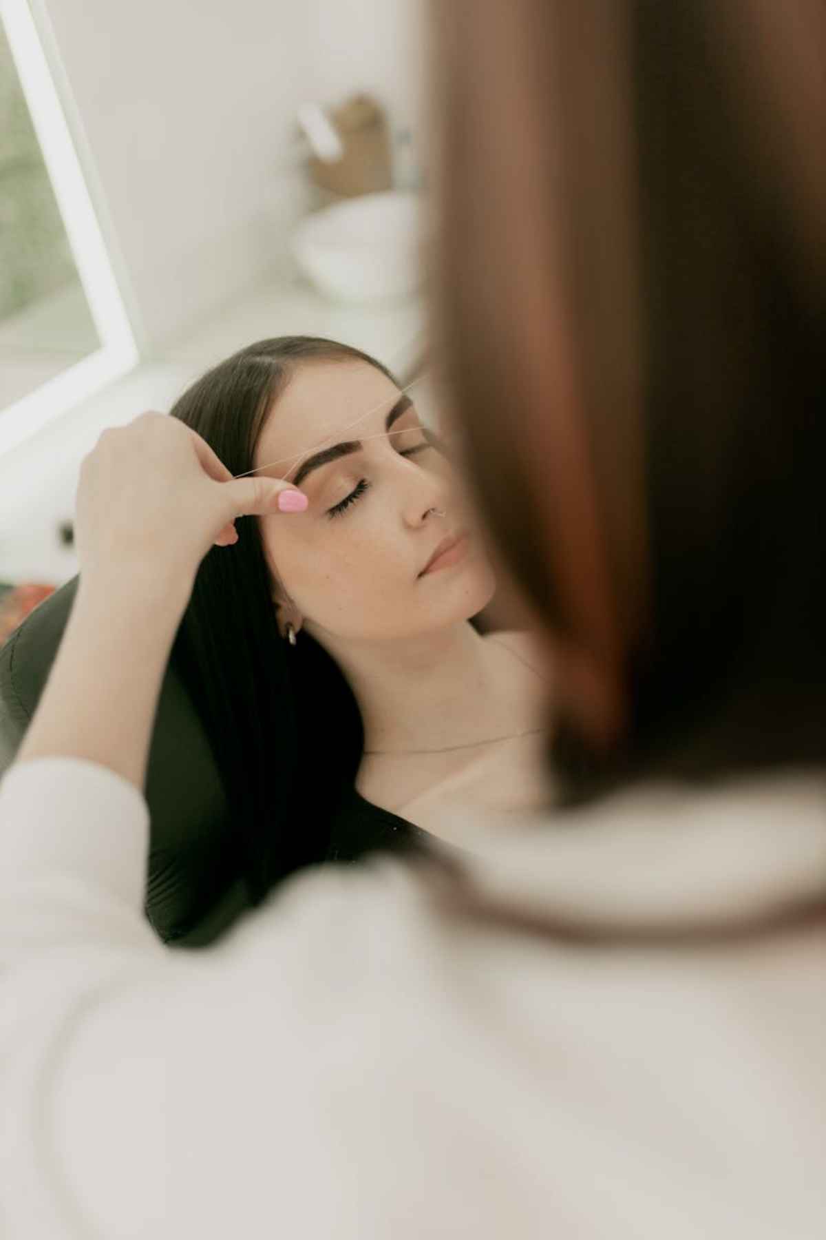 Beautician shaping young woman eyebrows in serene salon setting beauty
