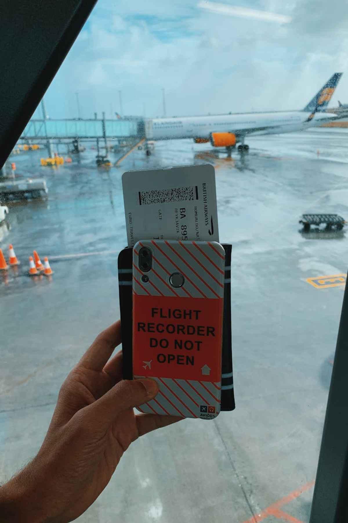 Hand holding a phone and boarding pass at an airport window with a plane on the tarmac