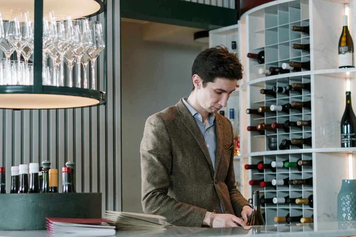 A sommelier stands at a chic wine bar surrounded by wine bottles and glasses.