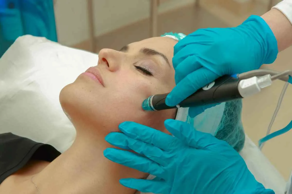 DiamondGlow vs HydraFacial: Is Diamond Glow Facial Better 1 A woman receiving a facial skincare treatment with a specialized device wearing protective gloves.