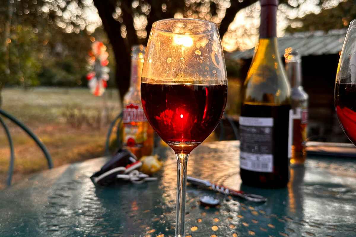 A glass of red wine on an outdoor table during sunset, surrounded by nature and evening glow.