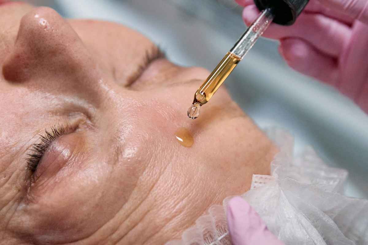 Senior woman receiving a facial serum treatment in a spa setting.