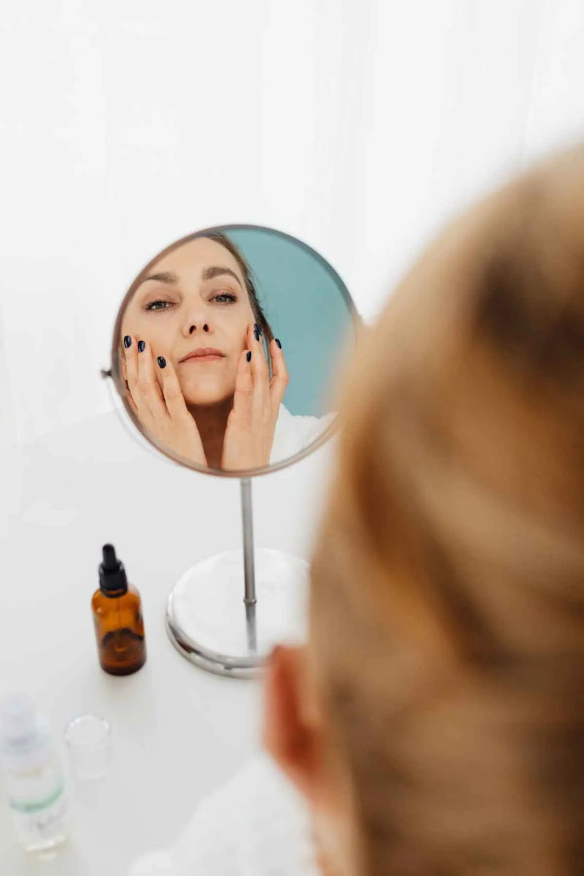 Adult woman applies skincare retinol serum looking in a mirror self-care routine