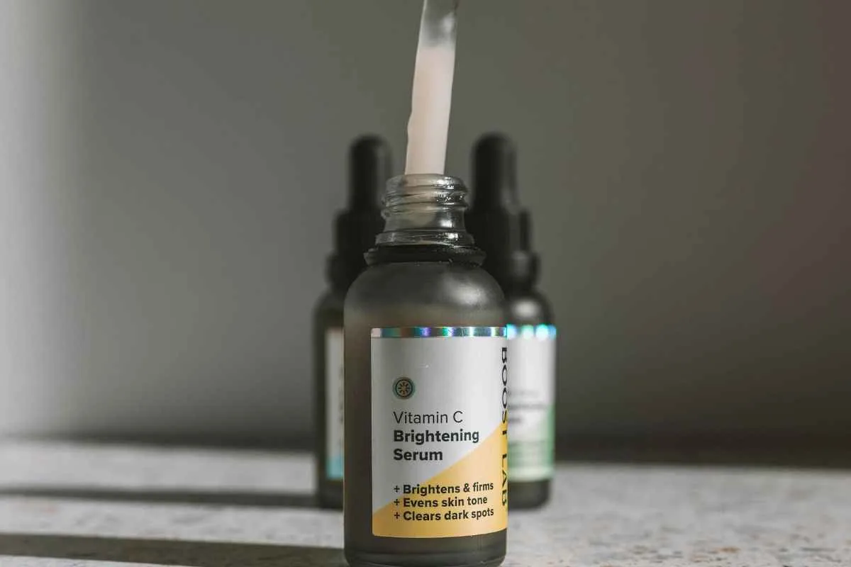 Close-up of a hand holding a dropper over a Vitamin C Brightening serum bottle on a textured surface.