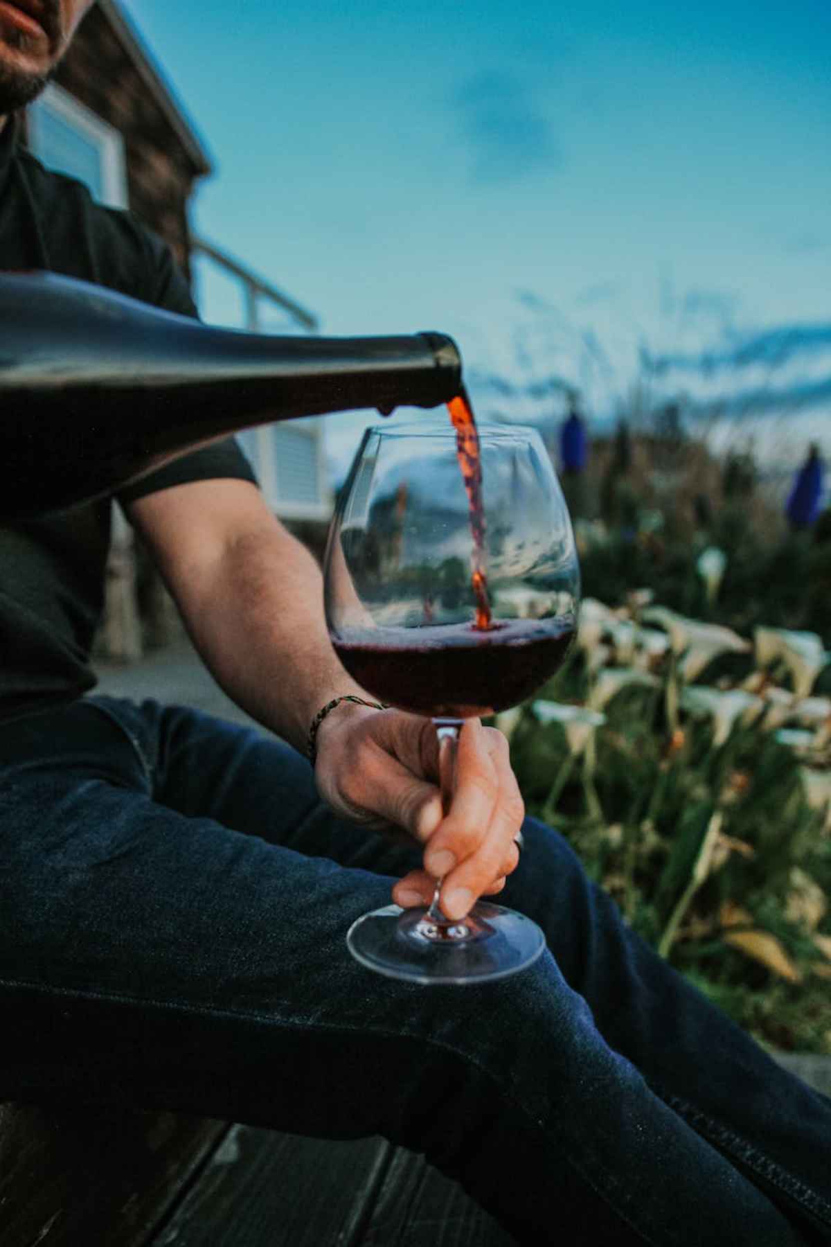 Pouring red wine into a glass while seated outdoors scenic vineyard view