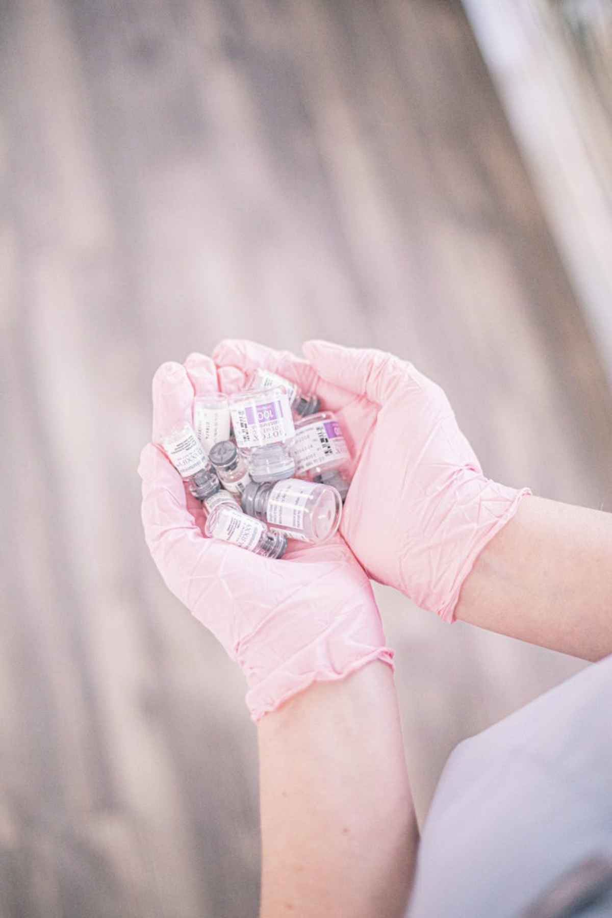 Aesthetic nurse wearing pink gloves holding vials of injectable treatments