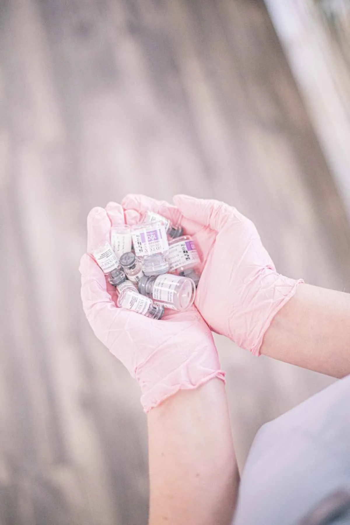 Aesthetic nurse wearing pink gloves holding vials of injectable treatments