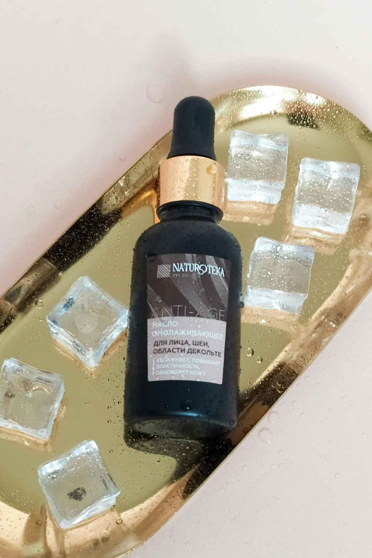 Close-up of a revitalizing serum bottle on a gold tray with ice cubes, conveying luxury skincare.