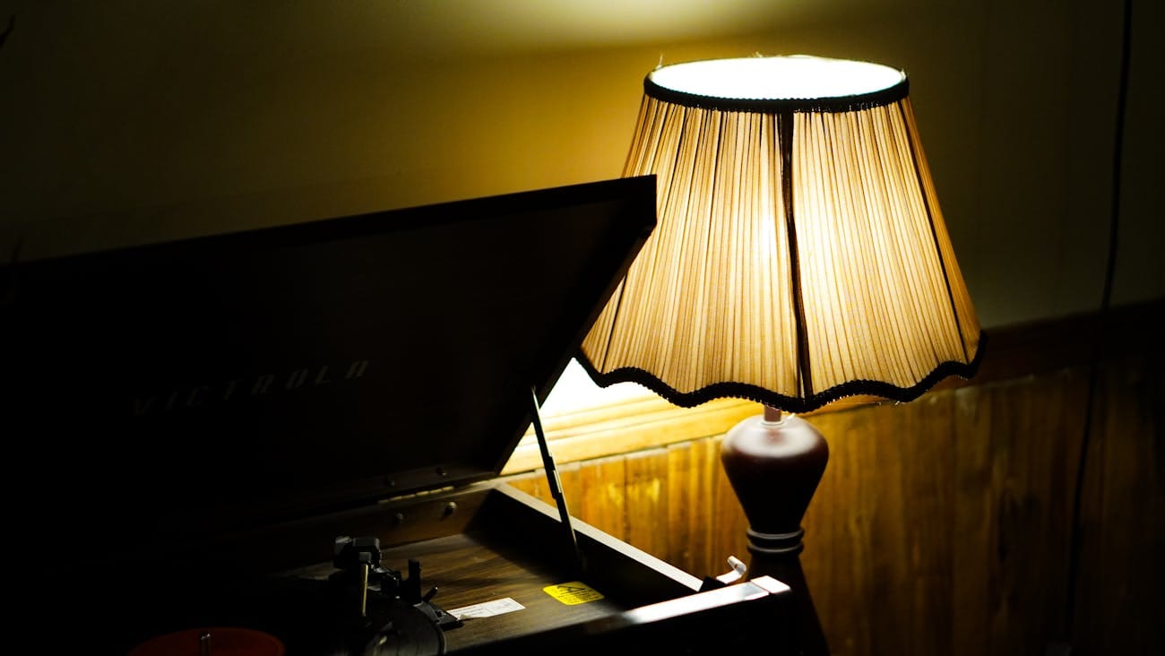 Warm glowing vintage table lamp with pleated shade casting soft amber light representing ambient lighting in a quiet luxury interior