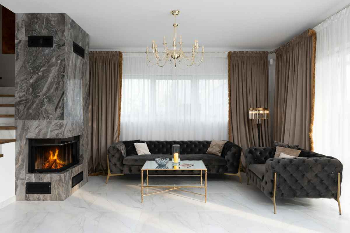Interior of modern living room with soft couches and side table placed near windows with curtains and burning fireplace at home