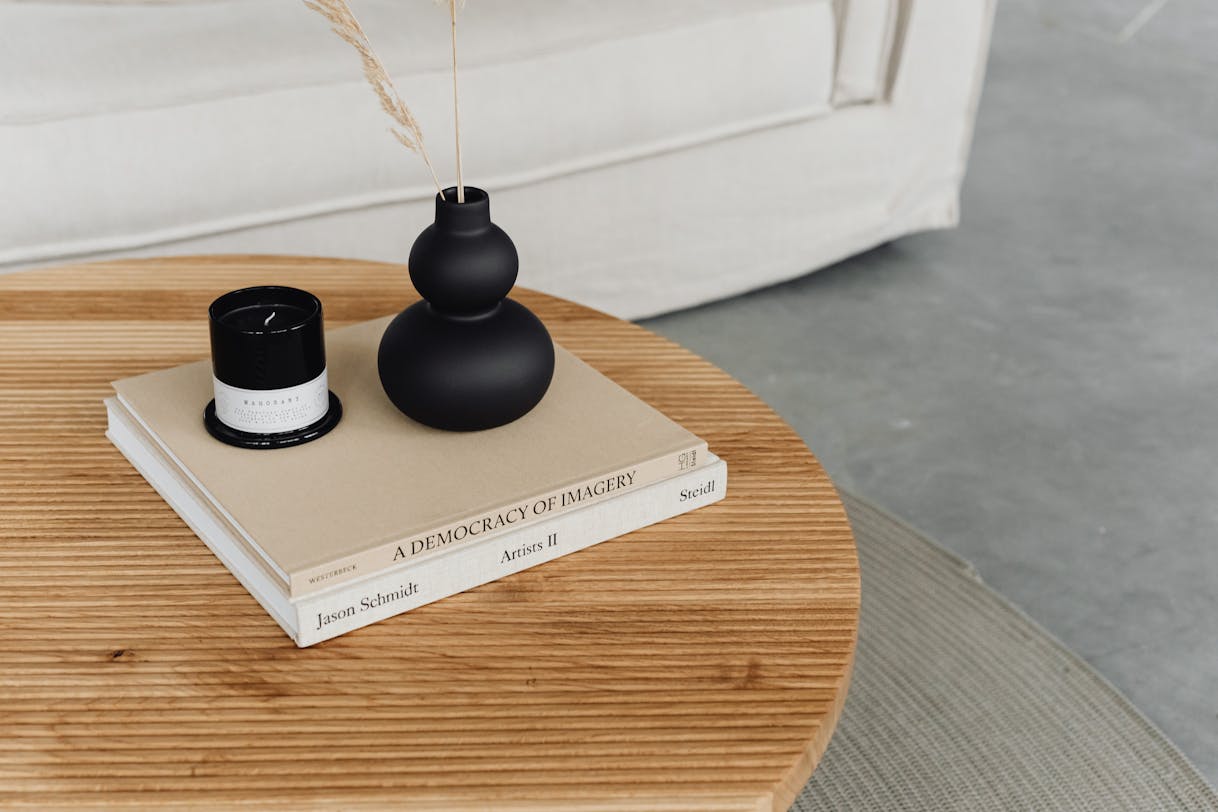 Curated coffee table styled with stacked art books a ceramic vase and a candle on a natural wood surface representing quiet luxury focal point design