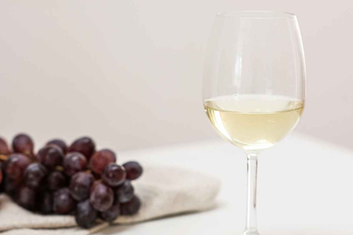 Elegantly presented white wine glass with a bunch of grapes on a white table.