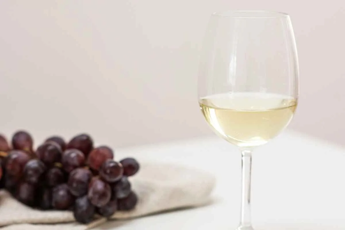 Elegantly presented white wine glass with a bunch of grapes on a white table.