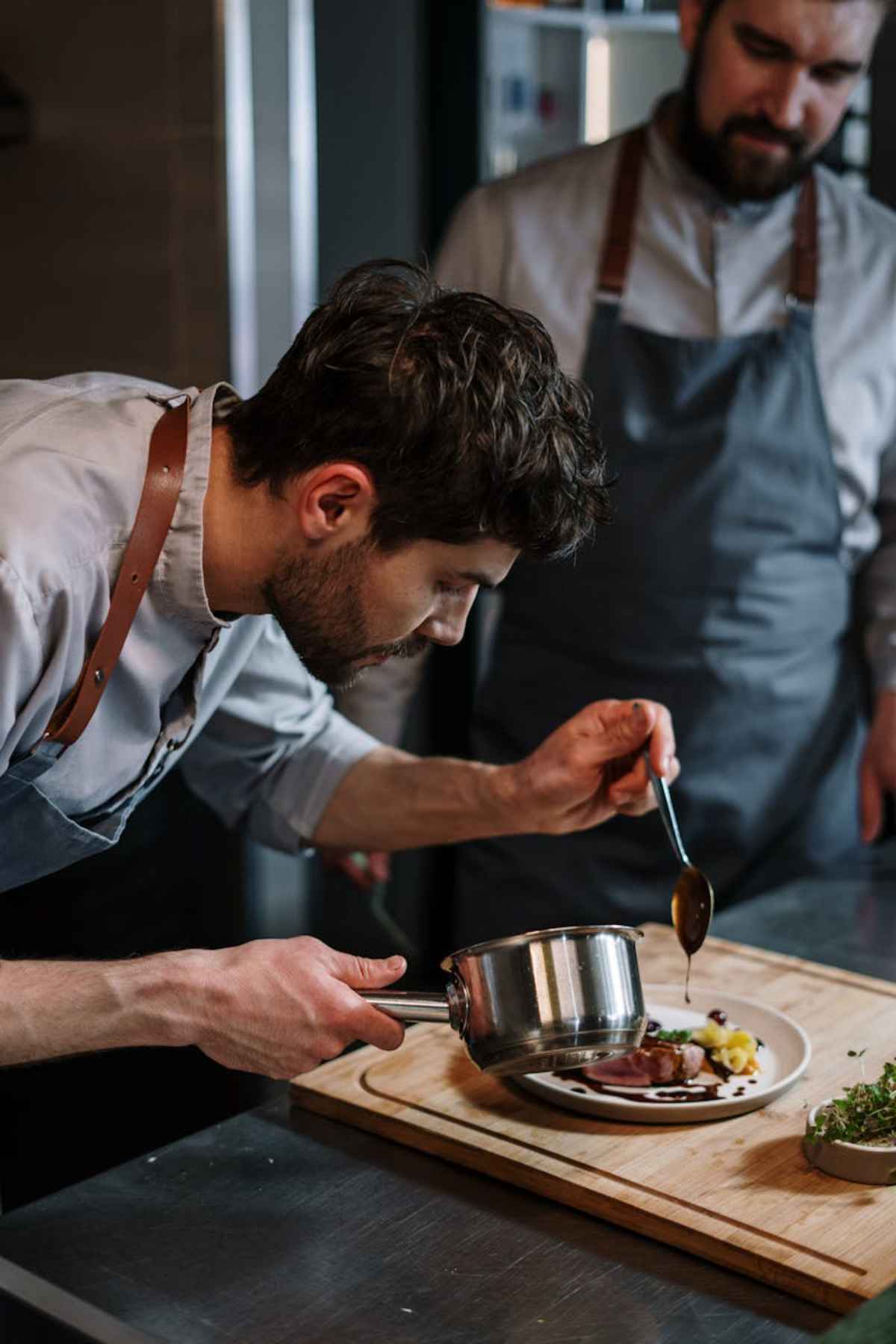 Chefs plating a gourmet beef dish in industrial kitchen fine dining