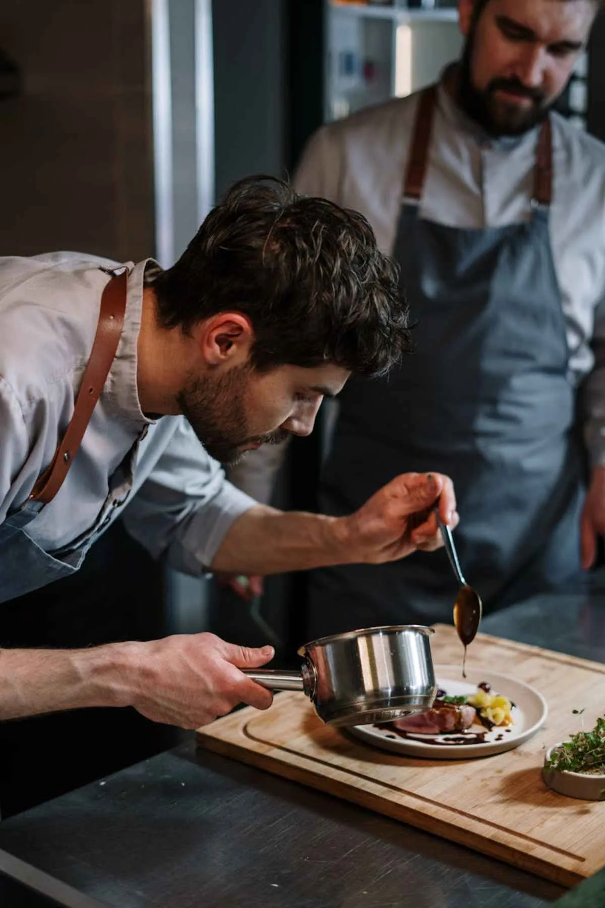 Chefs plating a gourmet beef dish in industrial kitchen fine dining