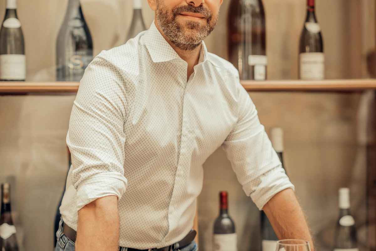 Syrah vs Merlot: Choosing the Perfect Red Wine for You 1 Smiling sommelier standing in a Paris wine bar with bottles and glasses.
