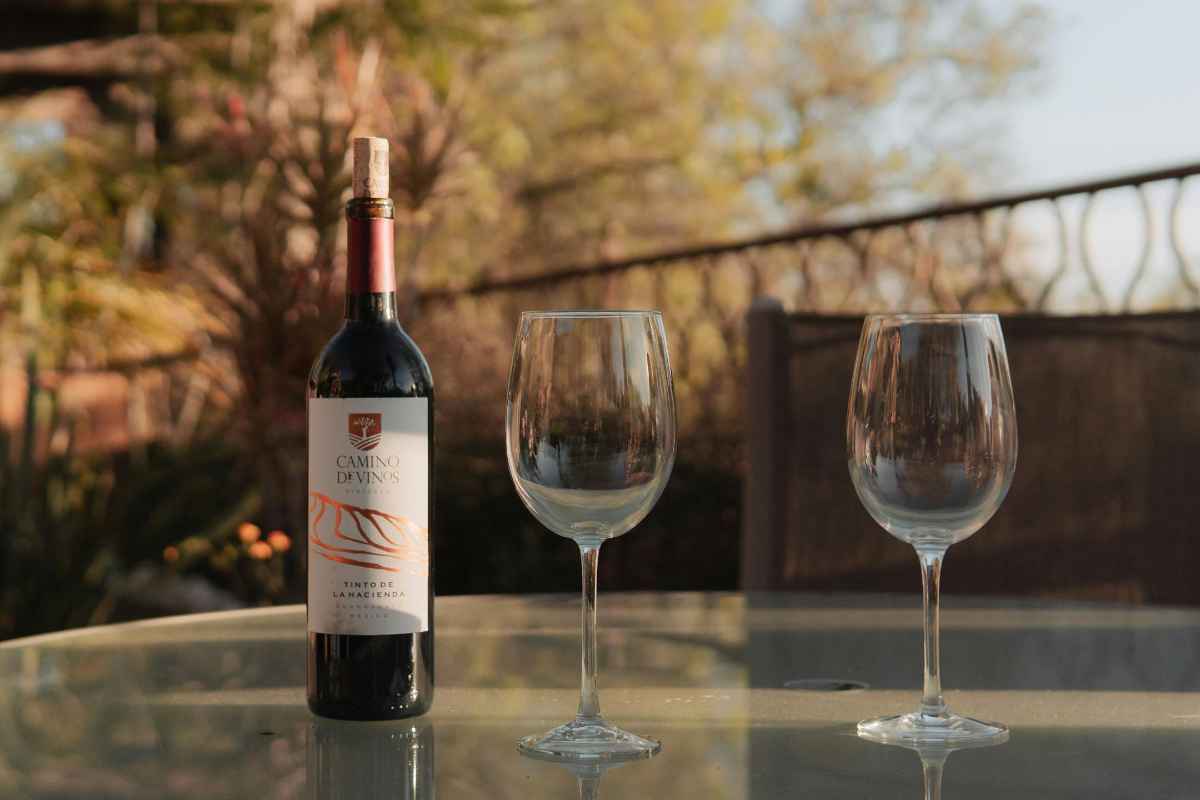 Red wine bottle and empty glasses on a glass table outdoors, inviting setting.