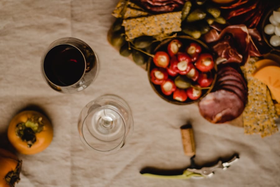 Elegant charcuterie board with red wine, cured meats and persimmons on a textured surface demonstrating classic wine and food pairings