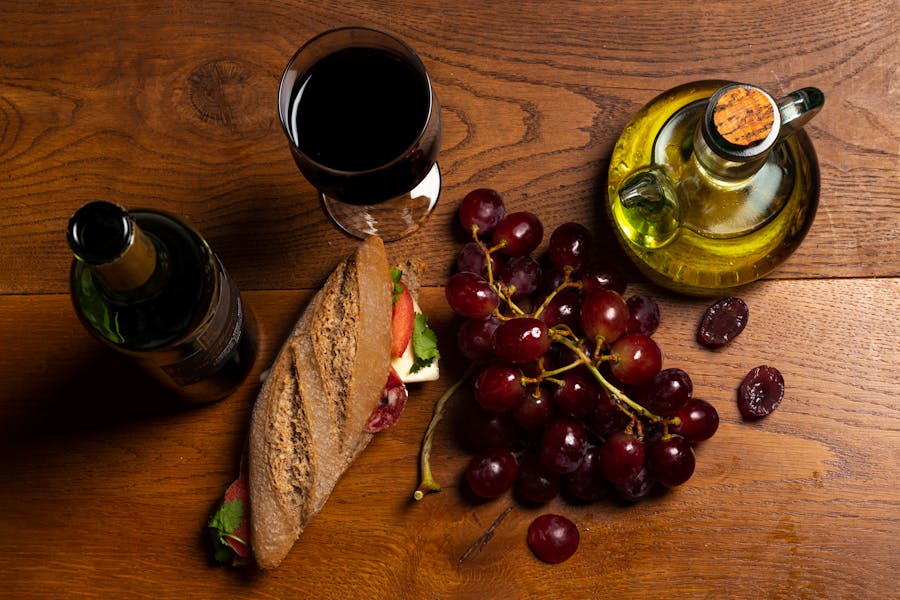 Top view of wine, baguette, grapes and olive oil on a rustic wooden table showing wine and food pairing by weight