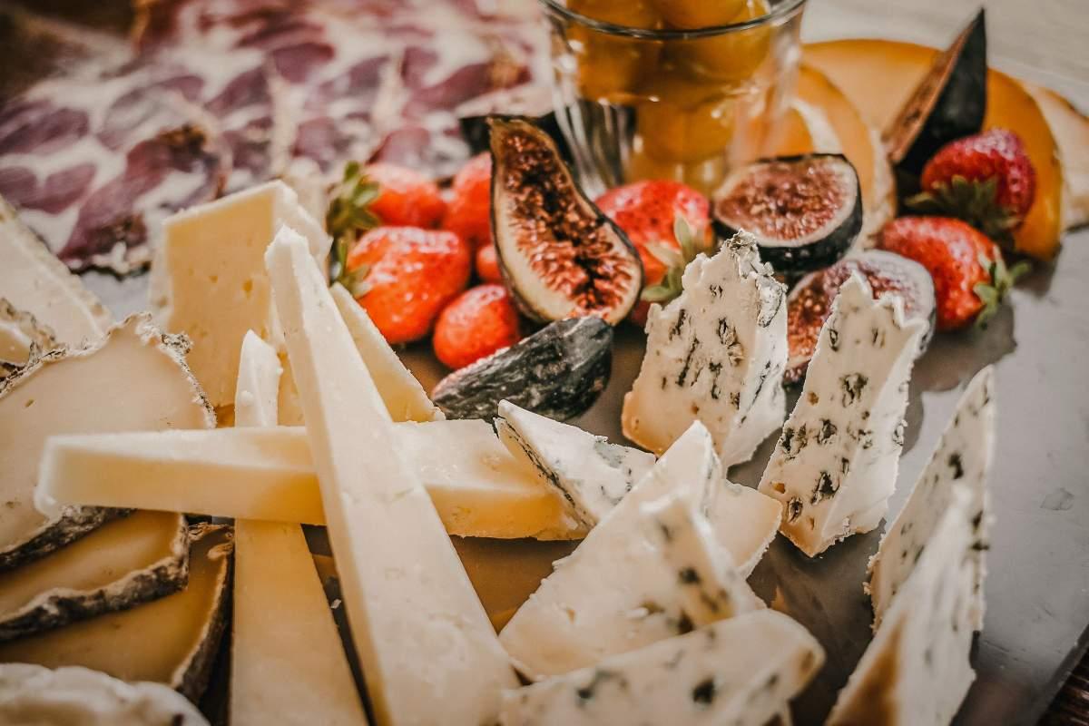 Cheese board with blue cheese wedges, hard cheese, fresh figs, and strawberries