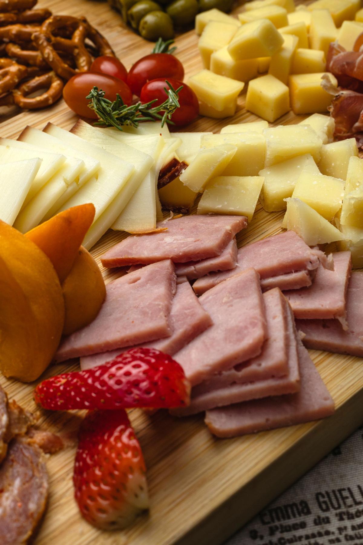 How to Make a Charcuterie Board: 7 Steps That Look Expensive 14 Wooden charcuterie board with sliced cheese, ham, salami, prosciutto, dried apricots, pretzels and cherry tomatoes