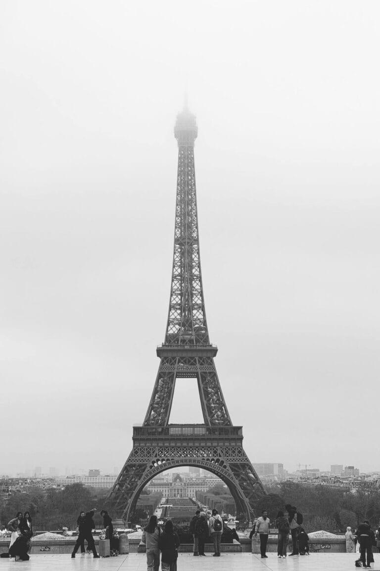Black and white photo of the Eiffel Tower in fog with visitors on a terrace in Paris