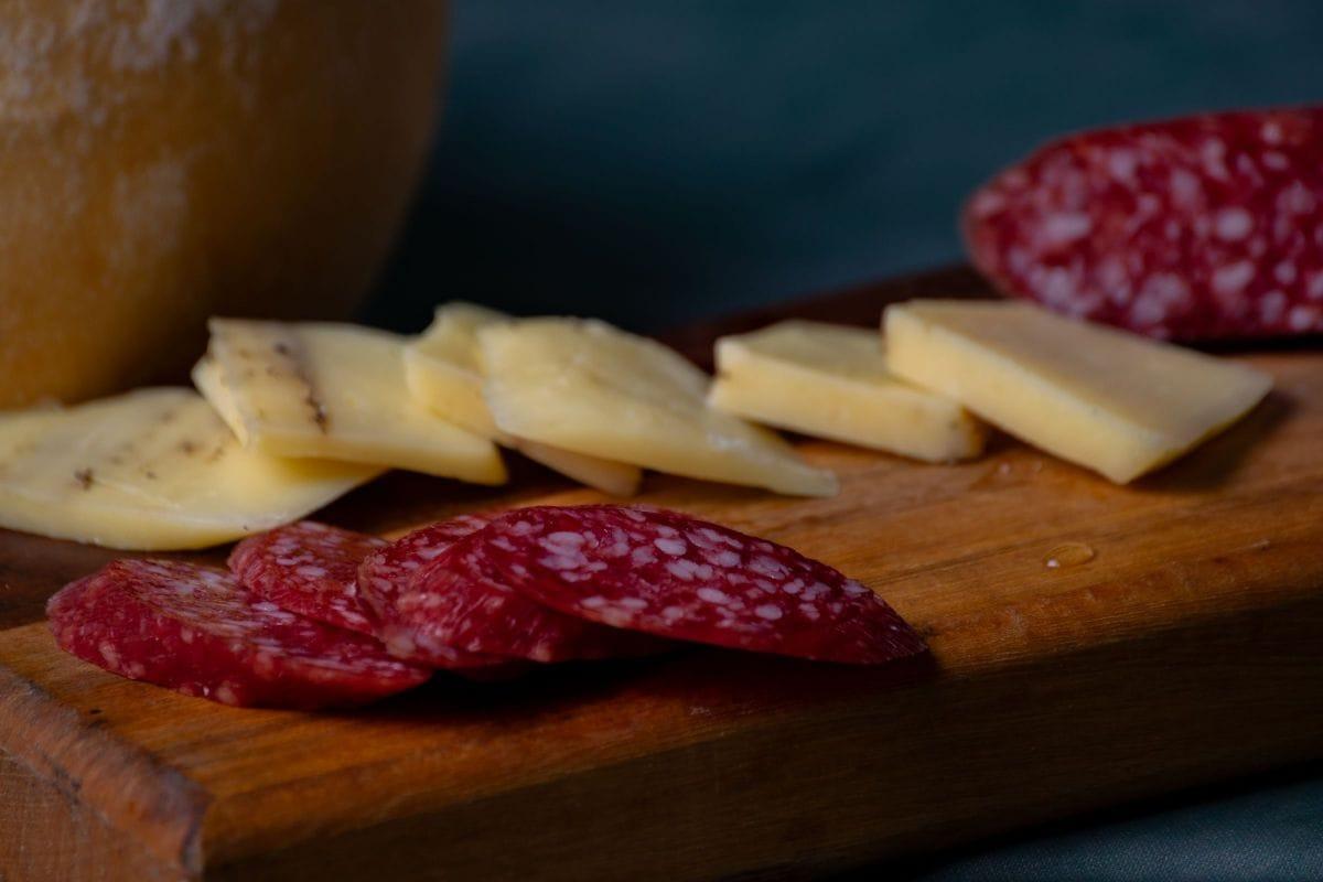 Sliced salami fanned beside thin slices of semi-hard cheese on a wooden board