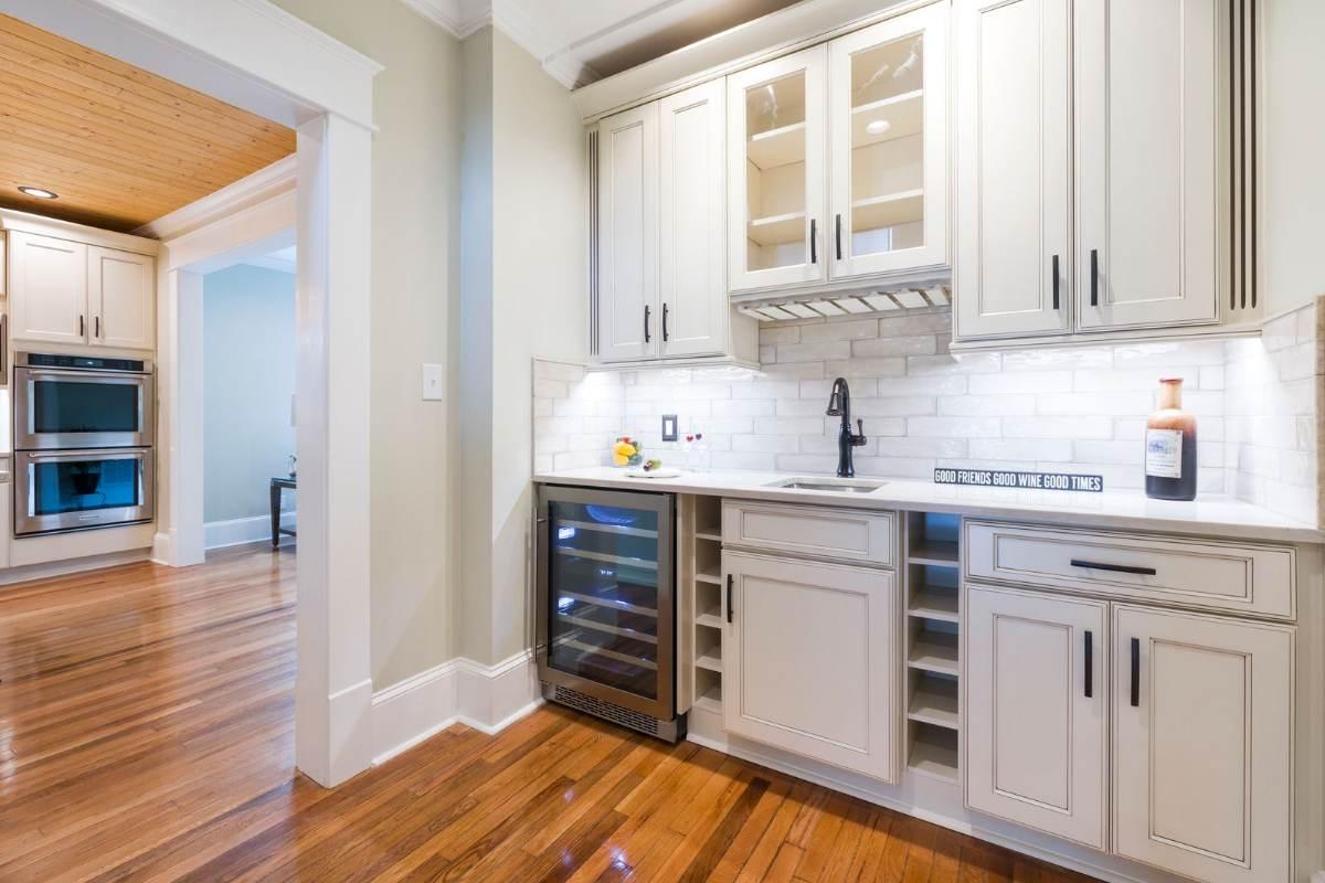 Under counter wine fridge built into a white kitchen bar area beside open wine rack cubbies