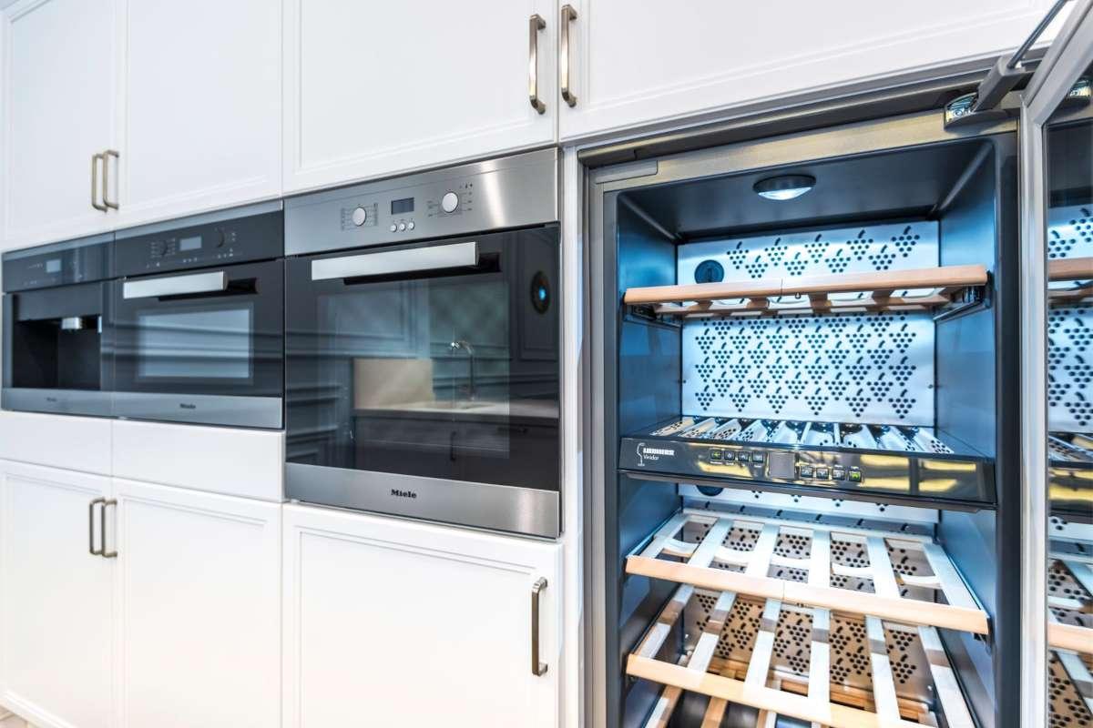 Gifts for Wine Lovers: 24 Picks Priced for 2026 4 Built in wine cooler with bottles on wooden shelves in a white kitchen