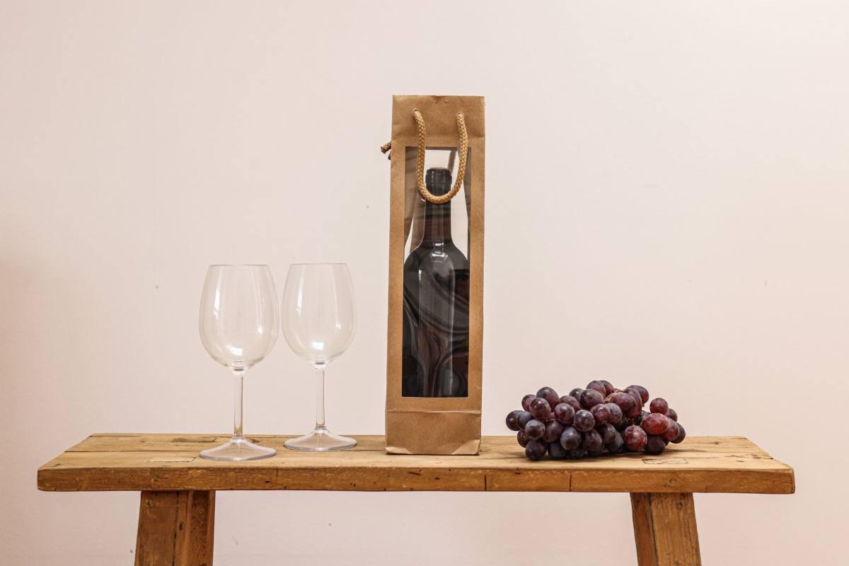 Gifts for Wine Lovers: 24 Picks Priced for 2026 5 Red wine in a paper gift bag with two wine glasses and grapes, one of the gifts for wine lovers